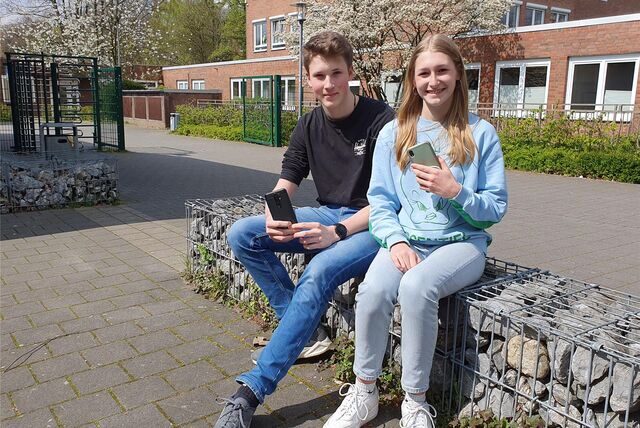 Ein Junge und ein Mädchen sitzen auf einer Mauer und halten Smartphones in der Hand