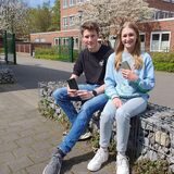 Ein Junge und ein Mädchen sitzen auf einer Mauer und halten Smartphones in der Hand