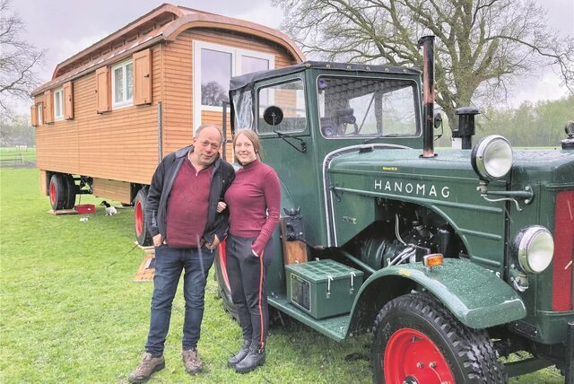 Das Elmenhorster Kronprinzenpaar Dieter Wember und Elena Schulze Langenhorst steht auf einer Wiese in Waltrop vor einem Trecker und einem Schaustellerwagen.