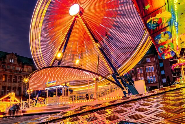 Das Riesenrad im Abendlicht vor dem spiegelnden Blech des Kinder-Fahrgeschäfts.