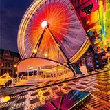 Das Riesenrad im Abendlicht vor dem spiegelnden Blech des Kinder-Fahrgeschäfts.
