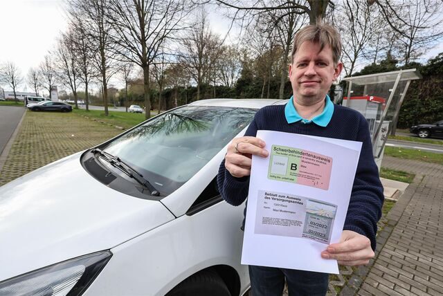 Carsten Stock mit seinem Auto und dem Muster eines Behindertenausweises auf dem P&R-Platz Hauptfriedhof.