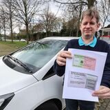 Carsten Stock mit seinem Auto und dem Muster eines Behindertenausweises auf dem P&R-Platz Hauptfriedhof.