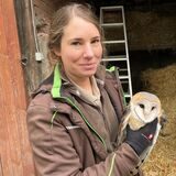Tierpflegerin Elisabeth Schüller hält eine Schleiereule in den Händen und lächelt in die Kamera.
