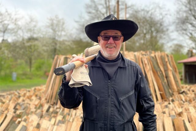 Der Köhler vor dem aufgeschichteten Holz des Meilers in der Haard