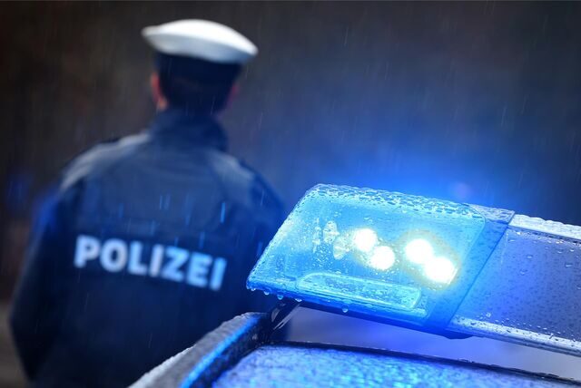 Ein Polizist steht im Regen vor einem Polizeiauto mit Blaulicht.