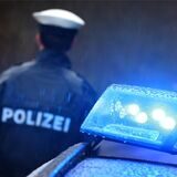 Ein Polizist steht im Regen vor einem Polizeiauto mit Blaulicht.