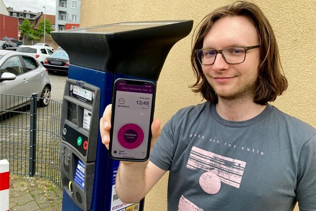 DM-Redakteur Benjamin Kübart steht mit einem Smartphone in der Hand vor einem Parkticket-Automaten.