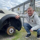 Gebrauchtwagenhändler Dietmar Mattukat kniet vor einem seiner Fahrzeuge. Vorsichtshalber hatte er den Reifen des Autos abgeschraubt, nachdem ihm andere Wagen gestohlen worden waren.