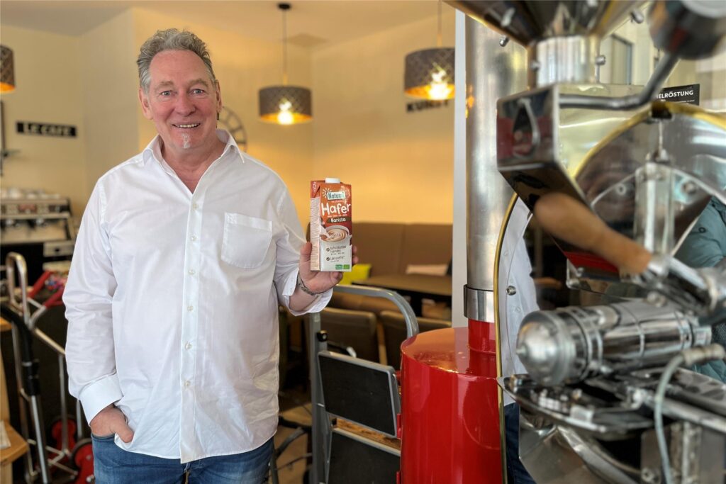 Ulrich Kellmann steht neben einer Röstmaschine und hält eine Tüte Hafermilch in der Hand.