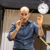 Rasmus Baumann hat seinen Dirigentenstab erhoben und schaut konzentriert in die Kamera.