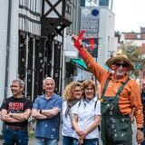 Mit einer roten Vorrichtung wirbelt ein Mann mit Strohhut und grüner Latzhose in Recklinghausen Seifenblasen in die Luft. Neben ihm stehen lachende Personen.