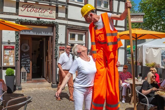 Eine Frau steht neben einem Stelzenläufer, der als Mitarbeiter der Müllabfuhr verkleidet ist.