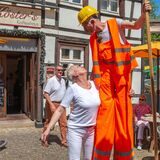 Eine Frau steht neben einem Stelzenläufer, der als Mitarbeiter der Müllabfuhr verkleidet ist.