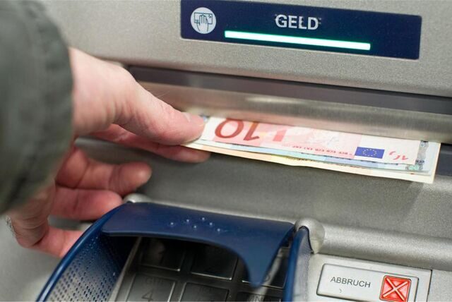 Eine Person zieht mit der linken Hand einige Geldscheine aus dem Schlitz eines Geldautomaten.