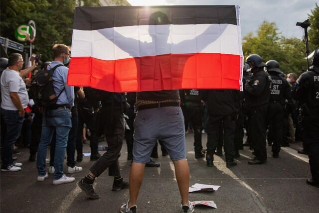 Die Rückansicht eines Mannes, der die schwarz-weiß-rote Reichsflagge in den Händen hält.