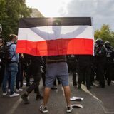Die Rückansicht eines Mannes, der die schwarz-weiß-rote Reichsflagge in den Händen hält.