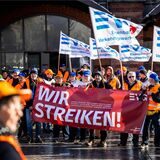 Demonstranten der Eisenbahn- und Verkehrsgewerkschaft (EVG) stehen mit Plakaten vor einem Hauptbahnhof.