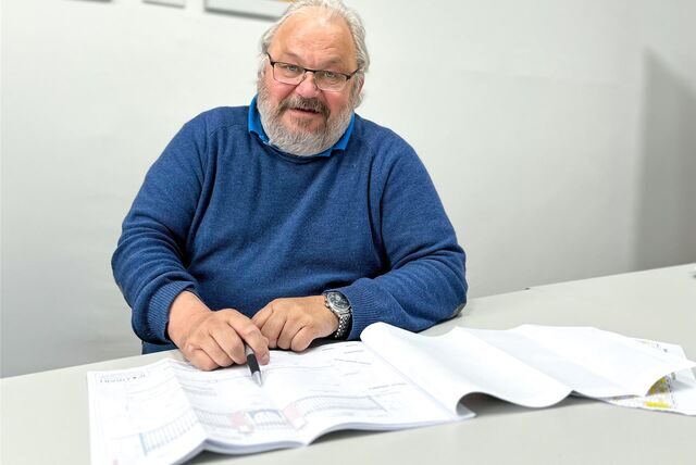 Wolfgang Bollrath sitzt an einem weißen Tisch und zeigt mit einem Stift auf den fertigen Entwurf.
