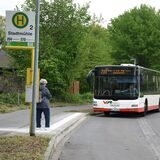 Eine Frau wartet an der Bushaltestelle auf den nahenden Bus.