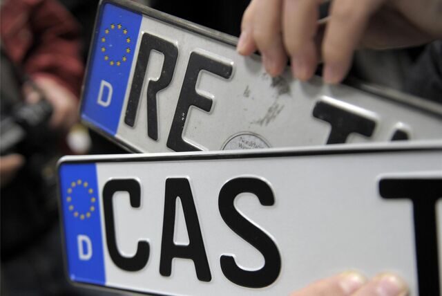 Ein Mann hält in der Zulassungsstelle in Marl die Nummernschilder mit den Kennzeichen RE und CAS hoch.