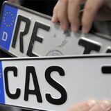 Ein Mann hält in der Zulassungsstelle in Marl die Nummernschilder mit den Kennzeichen RE und CAS hoch.