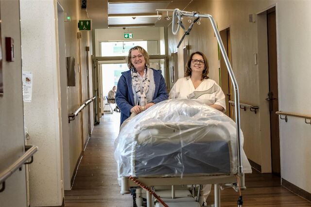 Ewa Monika Janocha und Stefanie Gross-Ulrich schieben ein Bett über den langen Krankenhaus-Flur.