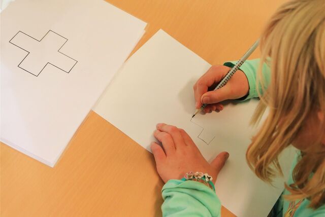Ein Kind malt ein Kreuz während einer Schuleingangsuntersuchung nach.