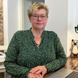 Ursula Wenig steht am Empfangstresen von ihrem Reisebüro. Vor ihr steht ihr Laptop und die Telefone liegen in Reichweite.