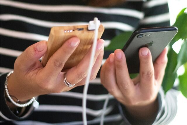 Eine Frau hält ein Smartphone in der einen und eine damit verbundene Powerbank in der anderen Hand.