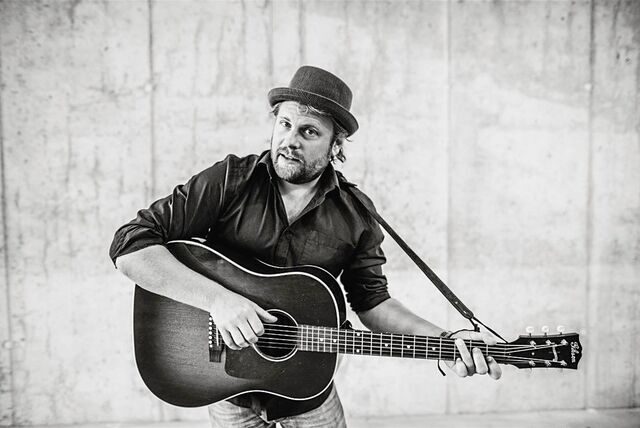 Musiker Sebel steht mit seiner Gitarre vor einer Wand.