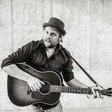 Musiker Sebel steht mit seiner Gitarre vor einer Wand.