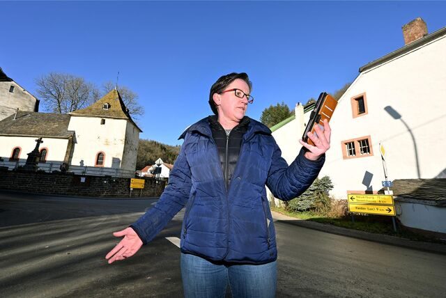 Ortsbürgermeisterin Stephanie Weiler hält im Ort schulterzuckend ein Smartphone, mit dem sie allerdings kein deutsches Mobilfunknetz erreichen kann.