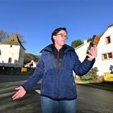 Ortsbürgermeisterin Stephanie Weiler hält im Ort schulterzuckend ein Smartphone, mit dem sie allerdings kein deutsches Mobilfunknetz erreichen kann.