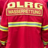Auf der rechten Seite des Bildes eine rote Jacke mit dem Schriftzug der DLRG, auf der linken Bildseite Niklas Tschäschke, Leiter für den Bereich Rettungsschwimmen der DLRG Recklinghausen