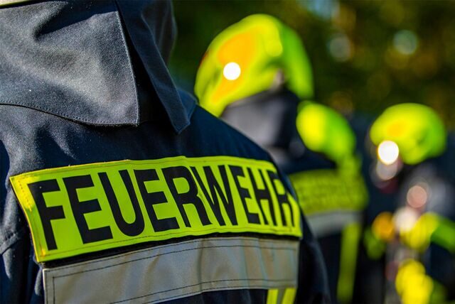 Auf dem Rücken eines Feuerwehrmannes steht das Wort „Feuerwehr“. Im Hintergrund sind andere Einsatzkräfte zu sehen.