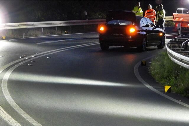 Ein Auto steht auf einer Autobahnauffahrt. Im Hintergrund stehen Polizei und Feuerwehr.