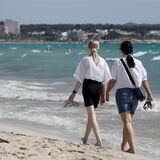Menschen gehen am Strand von Arenal entlang.