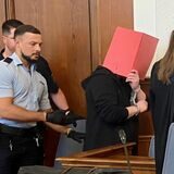 Der Angeklagte verdeckt sein Gesicht im Gerichtssaal mit einem Ordner