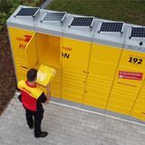 Ein DHL-Mitarbeiter legt ein Paket in eines der Fächer einer solarbetriebenen Packstation.