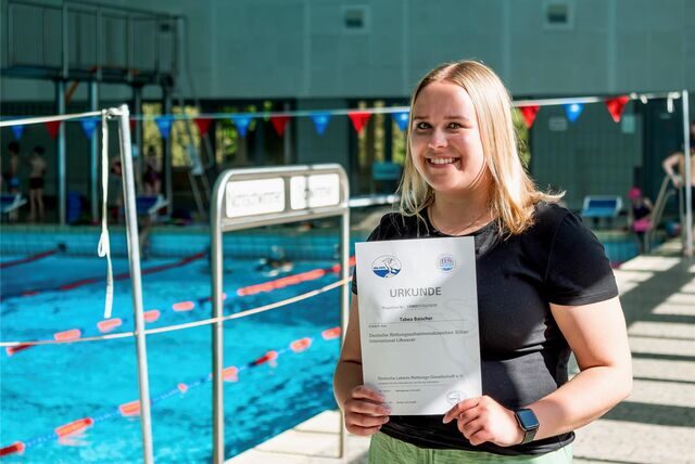 Tabea Baischer steht im Schwimmbad an der Herner Straße in Recklinghausen und hält eine Rettungsschwimm-Urkunde in den Händen.