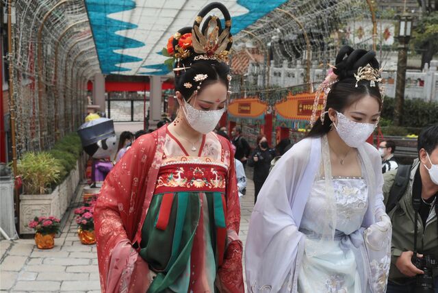 Junge Frauen in traditionellen chinesischen Kleidern und mit Mund-Nasen-Schutz gehen auf dem Gelände des taoistischen Wong Tai Shing-Tempels.