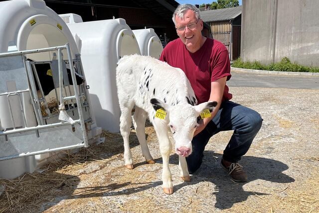 Dirk Feldhaus kniet neben einem Kalb auf seinem Hof.