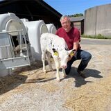 Dirk Feldhaus kniet neben einem Kalb auf seinem Hof.