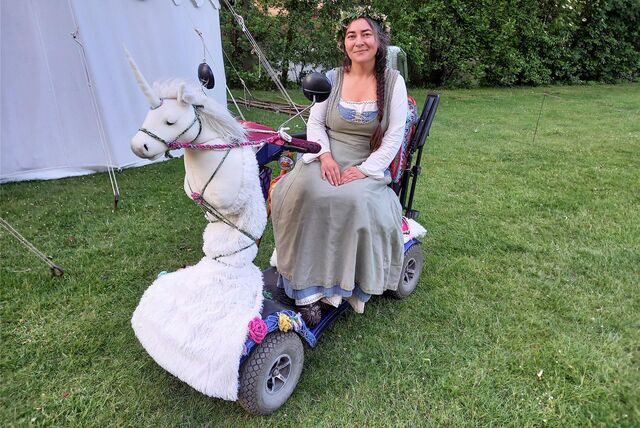 Eine Frau mit einem als Einhorn geschmückten Rollstuhl.