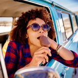 Eine Frau isst im Auto ein Eis am Stiehl und lehnt sich aus dem Fenster.