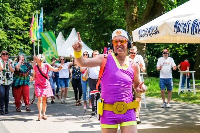 Ein Mann im pink-gelben Sportdress geht vor einer tanzenden Menge durch den Stadtgarten Recklinghausen.