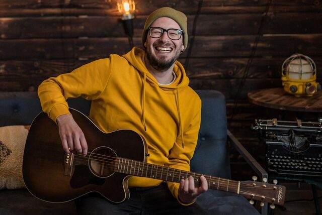 Der Künstler Philipp Artmann spielt Gitarre und lacht.