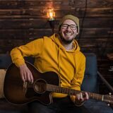 Der Künstler Philipp Artmann spielt Gitarre und lacht.