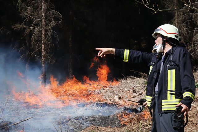 Ein Feuerwehrmann steht vor einem brennenden Waldstück bei Gummersbach.
